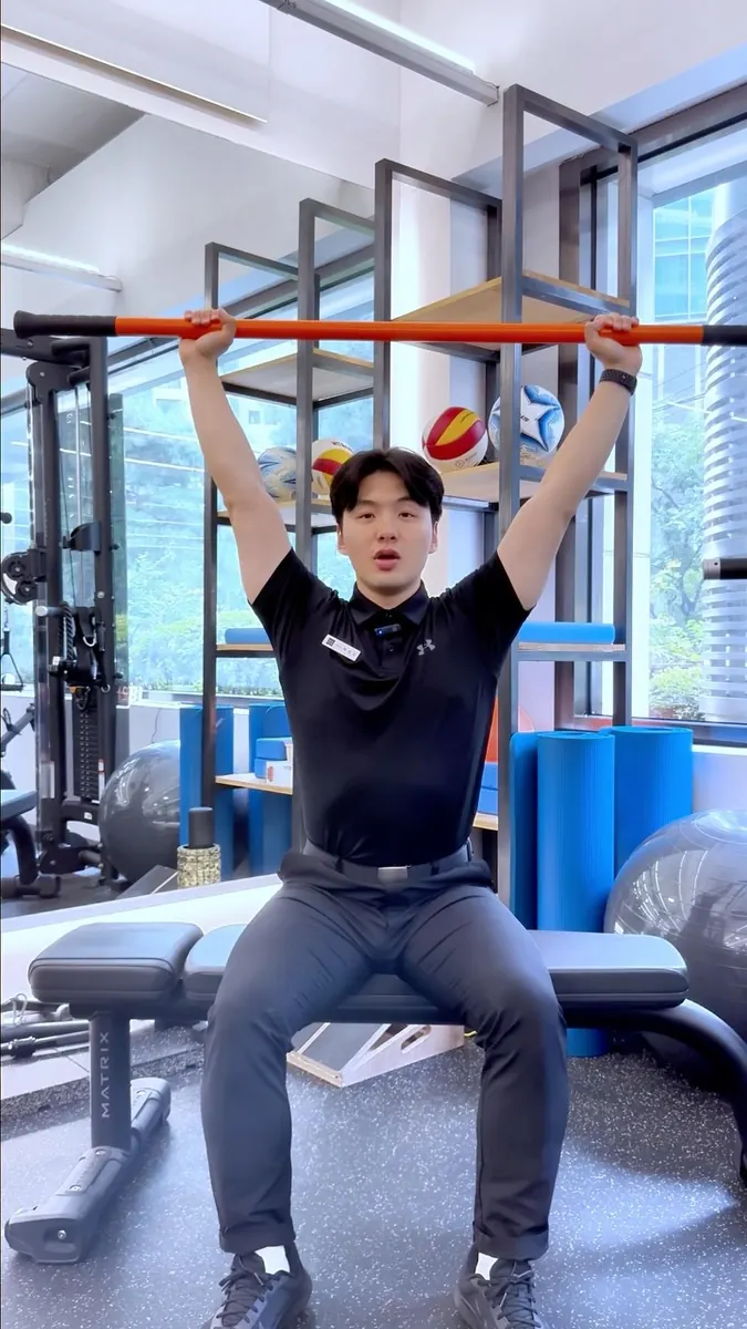 최형규 트레이너 · 앉은 자세 오버헤드 어깨 가동성 운동을 시연하는 모습
